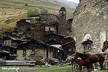 Vue d'un village à flanc de montagne, à droite à l'avant-plan des chevaux