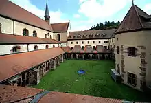 Photographie d'un cloître monastique, avec une église sur la gauche et le lavabo sur la droite.