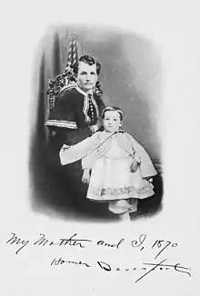 Photographie en noir et blanc d'une femme assise sur une chaise, devant laquelle se tient un petit garçon. Au pied de la photo, une mention manuscrite indique : « My mother and I, 1870 Homer Davenport ».