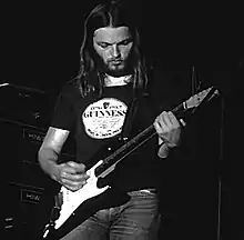 Image en noir et blanc d'un homme aux cheveux longs jouant de la guitare.