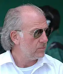 Photo de droit de David Richards, un homme à lunettes de soleil, chemise blanche, cheveux blancs et légèrement barbu