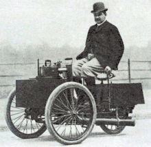 Photographie en noir et blanc d'un homme sur une voiture à trois roues.