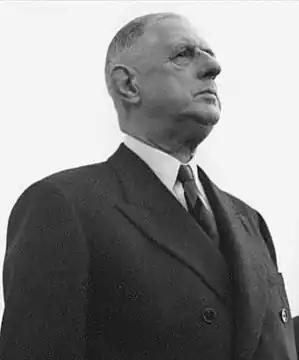 Photographie en noir et blanc, prise en contre-plongée et de droite, de Charles de Gaulle, vêtu d'un costume noir. Le cadrage de l'image rend le sujet impressionnant.