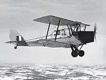 Photographie en noir et blanc d'un avion biplan en vol.