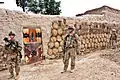 Des soldats américains patrouillant devant un qalat (en) afghan couvert de bouses de vache façonnées et séchées, en Afghanistan.