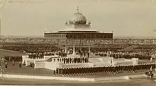 Vaste estrade blanche surmontée d'un chapiteau de style indien et entourée de milliers de soldats et de spectateurs