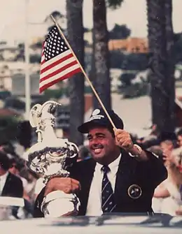 Dennis Conner, la Coupe de l'America sous le bras droit, un drapeau américain dans la main gauche.