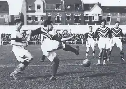 Photo en plein match. Sous le regard de ses coéquipiers et d'un adversaire, un joueur frappe dans la balle.