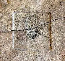 Detail plat d'une pierre beige de gris sur lequel est gravé un carré dans lequel se trouve gravés des caractères cunéiforme. La stèle est traversée d'une fente.