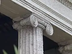 Photographie en couleurs rapprochée de l'extrémité d'une colonne en pierre cannelée et du chapiteau qu'elle supporte.