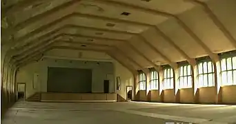 Un grand hall vide ; les murs et le toit font un demi-hexagone. Les fenêtres sont carrées. Une estrade est au fond du réfectoire.