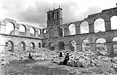 Photographie en noir et blanc d'un cloître dont il ne reste plus que les arcades sur deux niveaux, le reste du bâtiment ayant disparu.