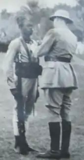 Photo d'un militaire noir au garde à vous, avec de Gaulle vu de dos, en casque colonial, qui lui épingle une décoration