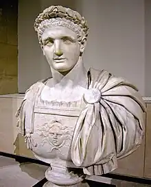 Buste d'un homme jeune, coiffé d'une couronne de laurier, portant un plastron décoré d'un soleil ; un drapé retenu par une pièce ronde lui couvre l'épaule droite.