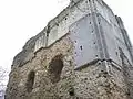 Photographie du mur d'un château fort depuis l'extérieur. Deux fenêtres sont visibles. Le mur est en mauvais état, une grande partie du parement a disparu.