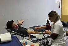 Homme jeune allongé sur un brancard, en train d'être perfusé par une infirmière.