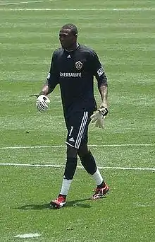 un joueur de football noir en survêtement noir courant sur une pelouse.