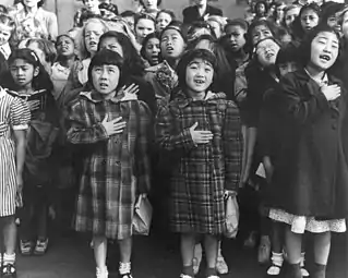 Les enfants de l'école publique de Weill, de la soi-disant colonie internationale, présentés lors d'une cérémonie de « serment d'allégeance au drapeau »(?) (flag pledge ceremony). Certains d'entre eux sont des évacués d'ascendance japonaise qui seront hébergés dans des centres d'autorité de relocalisation de guerre pendant toute la période. Avril 1942.