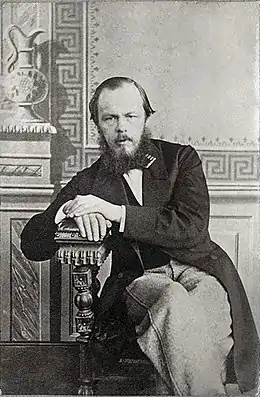 Photographie en noir et blanc de Dostoïevski âgé d'une quarantaine d'année, assis dans un fauteuil dans une pièce à la décoration néoclassique.