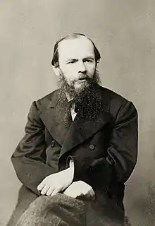 Portrait de l'écrivain, le front haut, avec barbe et moustache, assis, les bras croisés sur les cuisses.
