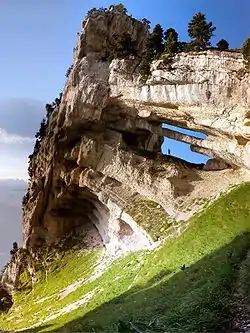 Promontoire rocheux percé par une double arche, avec une personne se tenant au milieu de la plus basse, en ombre chinoise.