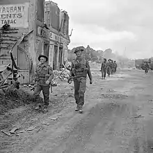 photo présentant des soldats anglais marchant sur une route au bord des ruines d'un village