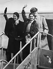 La famille MacArthur se trouvant au sommet de la rampe d'accès à un avion de passagers. Douglas MacArthur se tient à l'arrière de sa femme Jean et de son fils Arthur qui saluent.