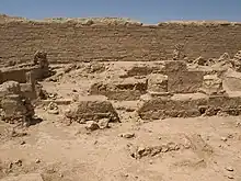 Photo en couleur. Dans le désert, des vestiges en pierres taillées sont à l'avant-plan.