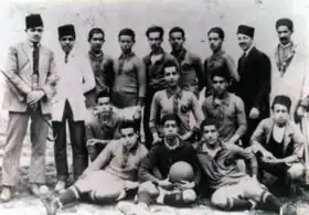 Photographie en noir et blanc d'une équipe de football, de face., avec des personnes debout ou assises.