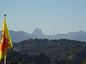 Paysage montrant un drapeau rouge et jaune sur la gauche et à l'arrière-plan des montagnes