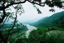 Photographie du système d'irrigation de Dujiangyan. Les voies d'eau sont visibles au fond d'une vallée bordée de montagnes verdoyantes sur la droite.