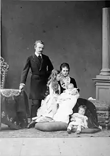 debout et revêtu d'une redingote sombre, le duc se tient aux côtés de sa fille aînée vêtue de clair et à la coiffure opulente de la duchesse assise portant sur les genoux sa fille nouvelle-née et aux pieds de laquelle Élisabeth est assise sur un coussin