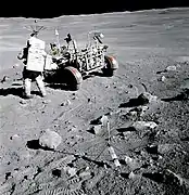 Photographie en couleur de Charles Duke en combinaison spatiale A7L à côté du rover lunaire.