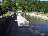 Le pont-canal de Dundas vue de l'extrémité est. La péniche sur l'image peut tourner à gauche vers des quais d'amarrage sur la seule section subsistante du canal à charbon du Somerset ou tourner à droite pour parcourir les derniers miles du canal vers la ville de Bath. Les murs du pont-canal sont visibles à gauche et à droite, la rivière et la voie ferrée ne sont pas visibles car bien en dessous.