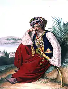 Un soldat égyptien, coiffé d'un turban et vêtu d'habits orientaux et colorés, assis sur une butte de terre, la main droite sur la pointe de sa moustache et l'autre main tenant son sabre.