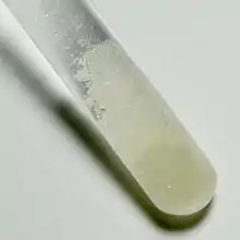 Photographie d'une cuillère de sulfate de dysprosium Dy2(SO4)3.