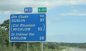 Panneau indicatif de la distance restante à parcourir pour atteindre les villes de Dublin, Wicklow et Arklow surmonté du sigle de l'autoroute irlandaise M11 ainsi que de celui de la route européenne 1