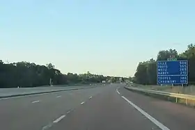 Vue d'autoroute avec panneau annonciateur de distance surplombé des panonceaux E21 et E17.