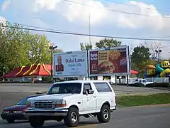 Un véhicule blanc roulant sur une route devant des panneaux publicitaires.
