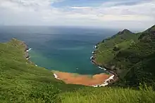 Vue depuis une hauteur, une baie entourée de collines avec des végétaux. L'eau au fond de la baie est rougeâtre.