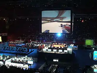 Grande salle plongée dans le noir, avec un écran géant affichant un jeu vidéo, où l'on ne distingue pas bien l'image.