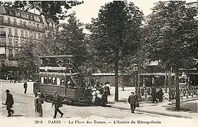 Photo légèrement sépia d'une place avec piétons, omnibus et entrée d'escalier ouvragée dans les arbres