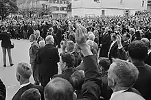 Photographie en noir et blanc d'un groupe d'homme sur une place publique en train de lever le bras droit.