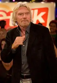 Photo de Richard Branson, aux cheveux blonds et longs, barbe blonde, devant une foule
