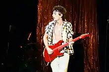 Photo d'un homme jouant d'une guitare rouge vif, la chemise ouverte et le torse nu