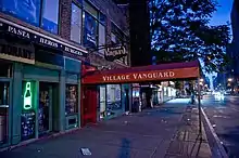 L'entrée du Village Vanguard, au lever du soleil. On voit l'auvent rouge du club qui avance sur la rue, sur lequel « Village Vanguard » est écrit, ainsi que le néon qui indique le nom du club. Le club est éteint et fermé, la rue est vide, le soleil commence à peine à se lever. On voit au loin des phares de voiture.