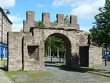 Photographie d'une arche de pierre surmontée de créneaux