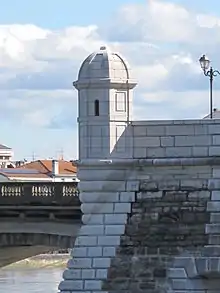 Photographie d’une échauguette de pierre blanche se détachant au-dessus d’un pont.