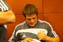 McCaw signe de la main gauche un ballon de rugby à XV présenté par un fan.