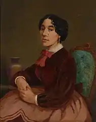Portrait à l'huile de Christiana Bannister. Elle est assise sur une chaise rembourrée et porte une jupe et un chemisier marron, avec un nœud rouge à la gorge. Elle joint ses mains et les pose sur une table à proximité.